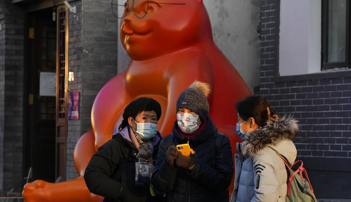 Warga yang mengenakan masker berdiri dekat patung kucing di Beijing, China, Selasa (11/1/2022. Beijing dalam siaga tinggi menjelang Olimpiade Musim Dingin saat China mengunci kota ketiga di tempat lain akibat COVID-19. (AP Photo/Ng Han Guan)