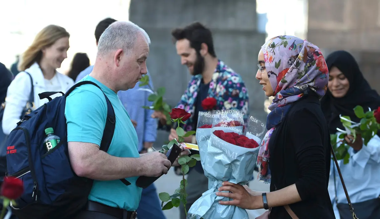 Seorang muslim membagikan bunga mawar disertai sebuah pesan kepada pejalan kaki di London Bridge, Minggu (11/6). Muslim Inggris membagikan ratusan mawar sebagai bentuk solidaritas menyusul teror London yang terjadi pekan lalu. (David Mirzoeff/PA via AP)