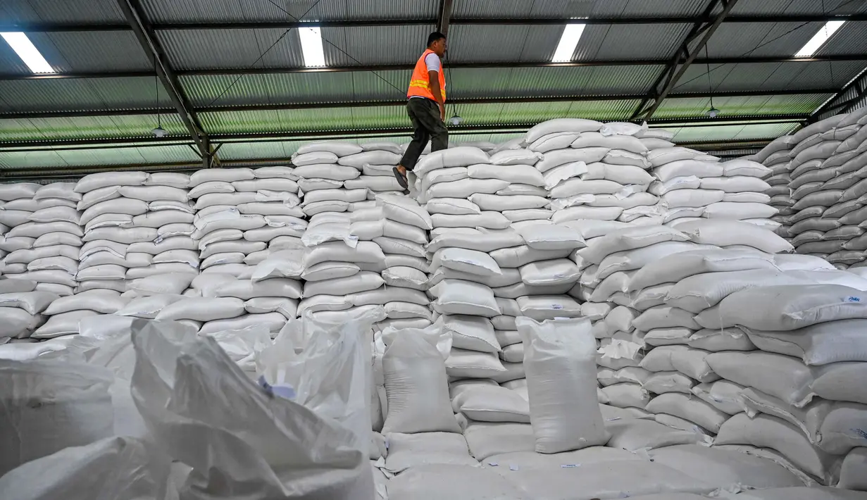 Melalui Perum Bulog, Badan Pangan Nasional (Bapanas) telah menambah pasokan ke tiga provinsi yang mengalami bencana banjir dan longsor Sumatra. Tampak dalam foto, seorang pekerja berjalan di atas tumpukan karung beras di gudang Badan Urusan Logistik (Bulog) di Lambaro, Provinsi Aceh pada 29 Desember 2025. (CHAIDEER MAHYUDDIN/AFP)