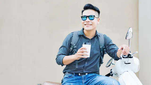 pria tersenyum pakai kacamata bersepeda motor vespa