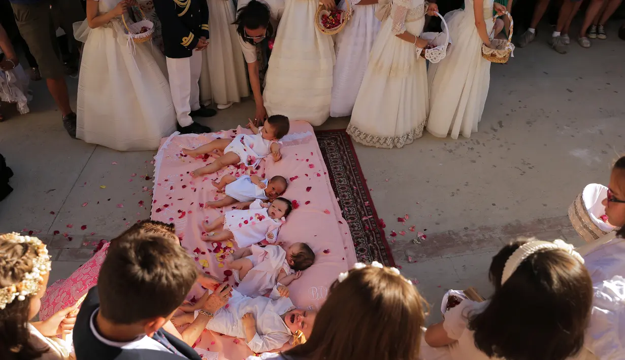 Bayi-bayi berusia hingga satu tahun ditaburi kelopak mawar sambil terlentang di atas matras usai dilompati pria berkostum setan selama festival melompati bayi (El Colacho) di desa Castrillo de Murcia, Spanyol, Minggu (18/6). (CESAR MANSO/AFP)