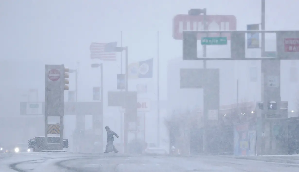 Seorang pria menyebrang jalan di bawah salju lebat saat terjadi badai salju di Jersey City, New Jersey (21/3). New Jersey telah mengumumkan keadaan darurat di mana sejumlah sekolah di Philadelphia ditutup. (AP/Julio Cortez)