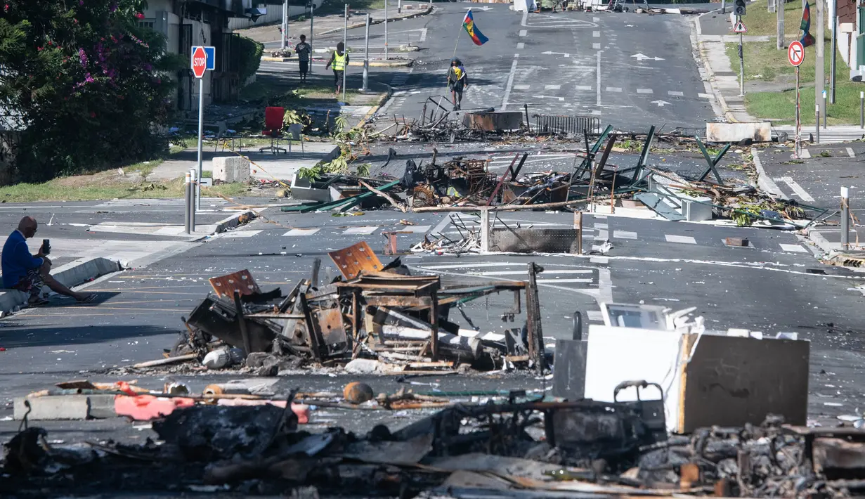 Sebuah jalan diblokir oleh puing-puing dan barang-barang yang terbakar pasca-kerusuhan semalam di distrik Magenta di Noumea, wilayah Pasifik Prancis di Kaledonia Baru, pada 18 Mei 2024. (Delphine Mayeur/AFP