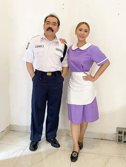 Adam Suseno kali ini menjadi petugas keamanan alias sekuriti di sebuah rumah mewah. Ia tampil rapi dengan kemeja putih lengan pendek dan celana panjang biru dongker. Sang Ratu Ngebor rupanya jadi asisten rumah tangga dengan atasan dan rok warna kecubung. Agar tak terkesan monoton, pada bagian kerah, lengan, dan celemeknya diwarnai putih. (Foto: Dok. Instagram @inul.d)