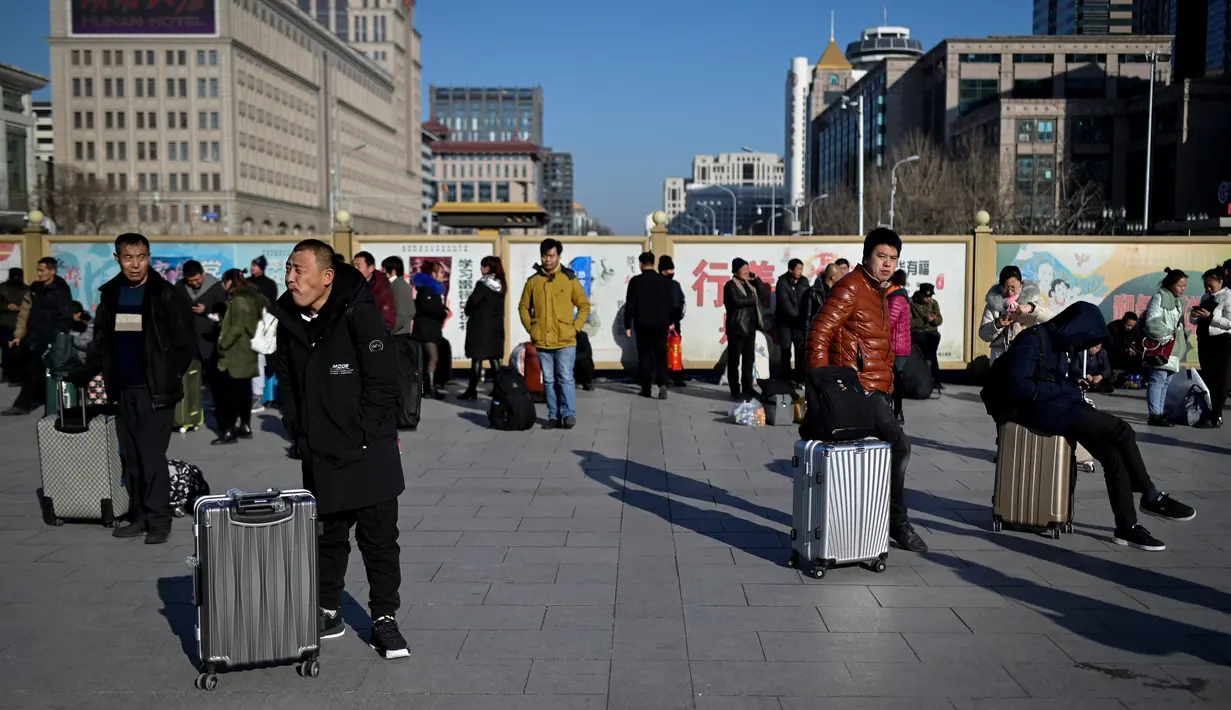 Pelancong menunggu jadwal keberangkatan kereta mereka di luar pintu masuk stasiun kereta api Beijing, Jumat (10/1/2020). Puluhan ribu warga China telah memulai migrasi manusia terbesar di dunia meninggalkan kota-kota besar menuju kampung halaman untuk merayakan Tahun Baru Imlek. (WANG ZHAO/AFP)