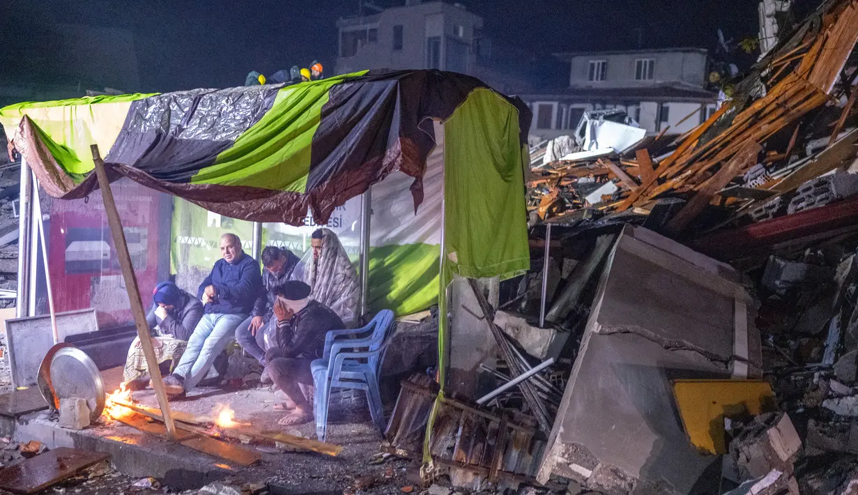 Orang-orang beristirahat dekat api unggun di samping reruntuhan setelah gempa, Hatay, Turki, 6 Februari 2023. Gempa magnitudo 7,8 yang melanda Turki dan Suriah menewaskan lebih dari 3.000 orang dan meratakan ribuan bangunan. (BULENT KILIC/AFP)