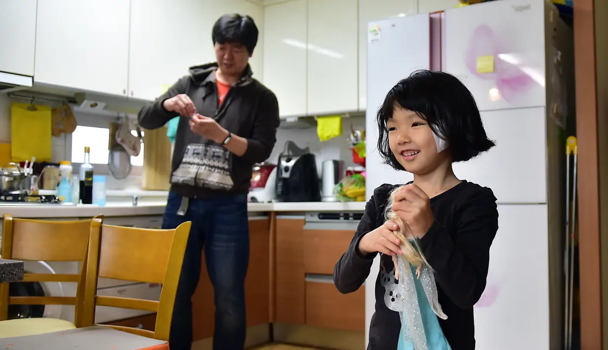 Kim Jin-Sung saat berada di dapur dan terlihat putrinya Na-Eun bermain dengan boneka di apartemen mereka di Seoul. Sebuah ide yang tak biasa dimana anak sehari-hari dapat diurus oleh seorang pria yang merupakan tanggung jawab wanita. (AFP PHOTO/JU)