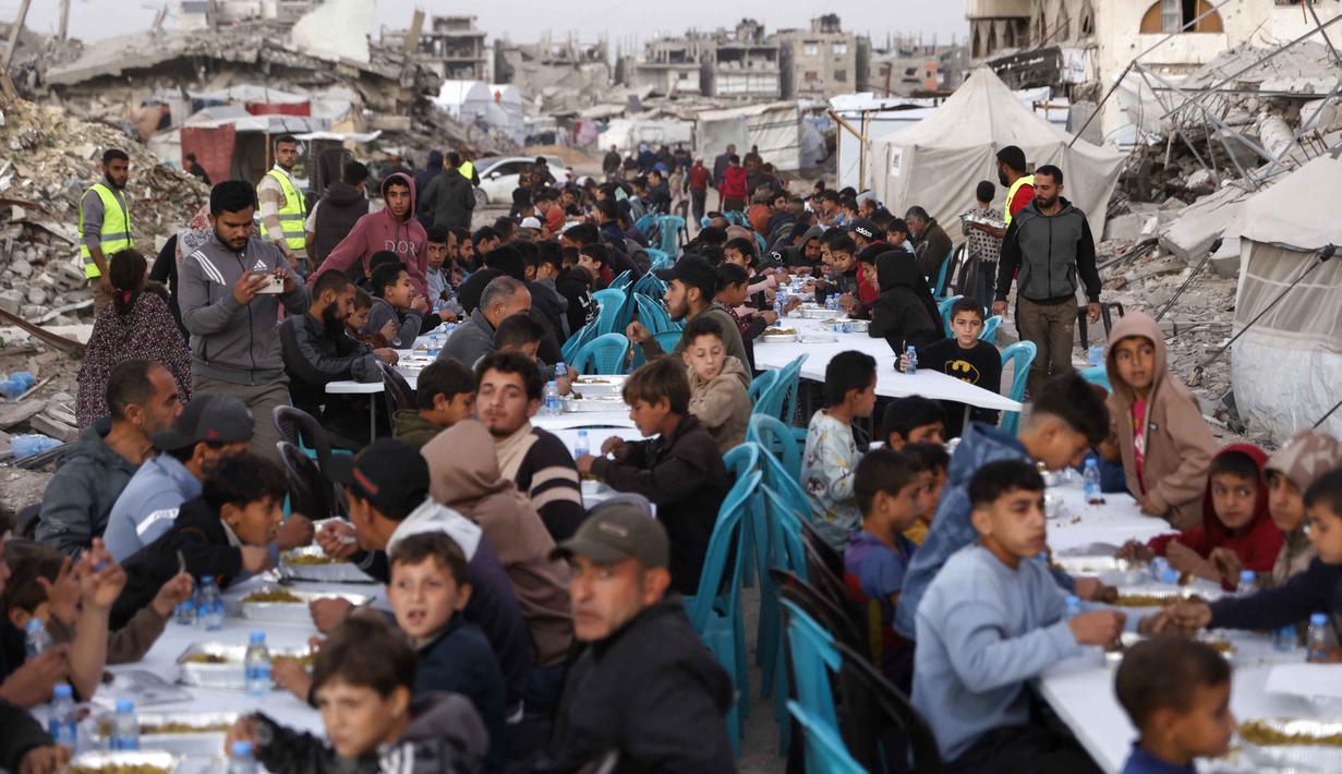Untuk diketahui, acara buka puasa bersama ini diselenggarakan oleh Yayasan IHH Turki, sebuah organisasi non-pemerintah (NGO) konservatif asal Turki yang berbasis di Istanbul dan aktif di lebih dari 120 negara sejak 1992. Tampak dalam foto, warga Palestina berkumpul untuk berbuka puasa bersama yang diselenggarakan oleh Yayasan IHH Turki, di tengah reruntuhan bangunan yang hancur di Kota Gaza pada Rabu 18 Februari 2026. (Omar AL-QATTAA/AFP)