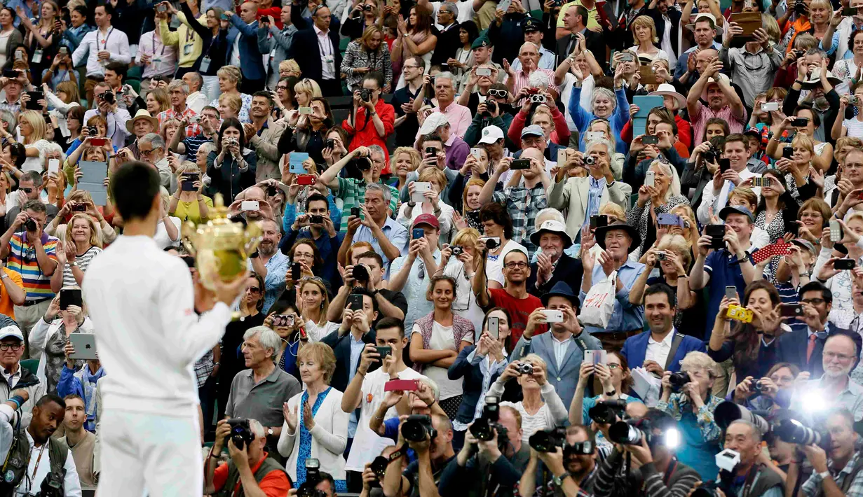 Petenis Serbia, Novak Djokovic menunjukkan trofinya ke para fans setelah mengalahkan petenis Swiss, Roger Federer di babak final tunggal putra Wimbledon 2015, London, Minggu (12/7). Ini adalah gelar Wimbledon ketiga bagi Djokovic. (REUTERS/Stefan Wermuth)