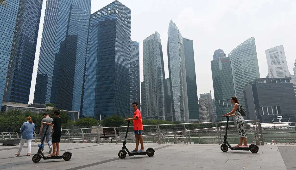 Orang-orang menggunakan skuter skate di sepanjang Marina Bay ketika bangunan diselimuti kabut asap di Singapura (13/9/2019). Titik api di hutan hujan Indonesia telah melonjak tajam, data satelit menunjukkan pada 12 September, menyebarkan kabut asap di Asia Tenggara. (AFP Photo/Roslan Rahman)