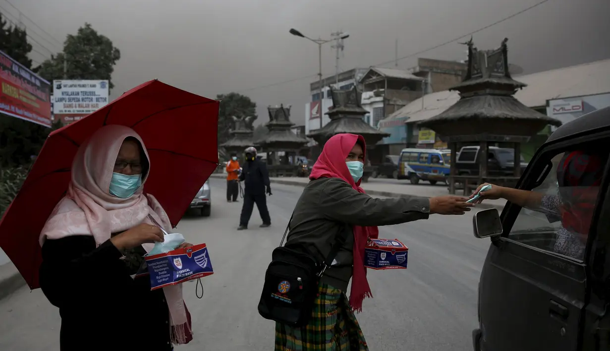 Relawan membagikan masker kepada pengendara kendaraan di kawasan Berastagi, Karo, Sumatera Utara, 25 Juni 2015. Debu vulkanik akibat erupsi Gunung Sinabung masih menutupi sebagian Kota Berastagi. (REUTERS/Beawiharta)