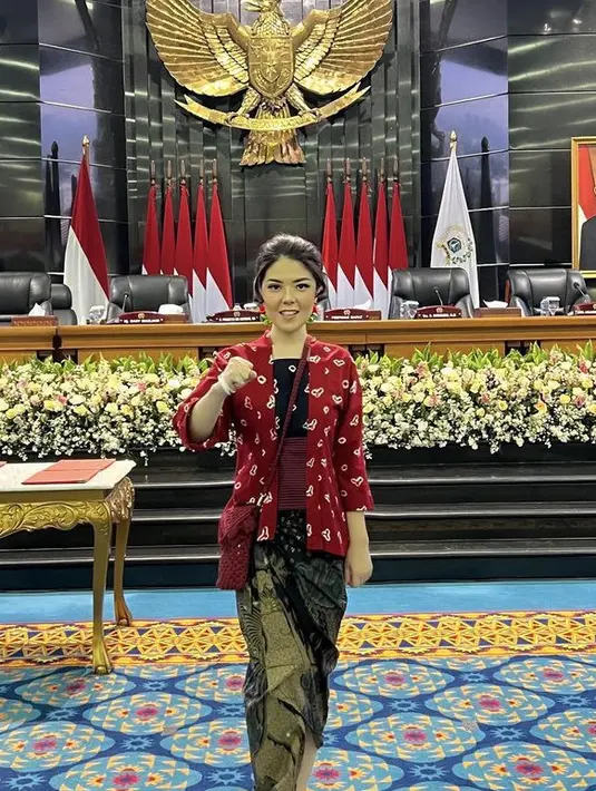 Melengkapi tampilannya dengan bawahan kain lilit batik. Sambil membawa mini bag maroon berbahan knit. [@tinatoon101]