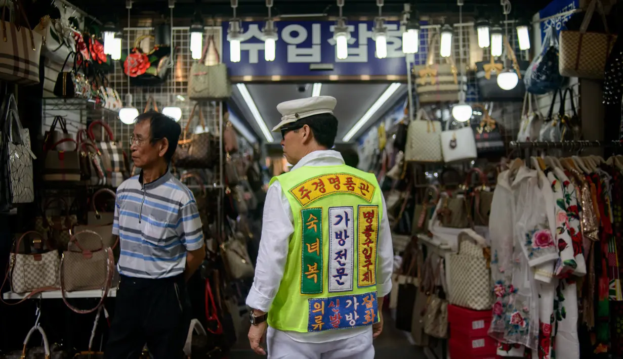 Seorang pria mengenakan rompi saat mengiklankan pakaian, sepatu, dan tas di luar sebuah toko di pasar Namdaemun di Seoul (2/7/2019). Dibangun pada tahun 1946, Pasar Namdaemun merupakan salah satu pasar tradisional yang terbesar di Korea. (AFP Photo/Minji Suh)