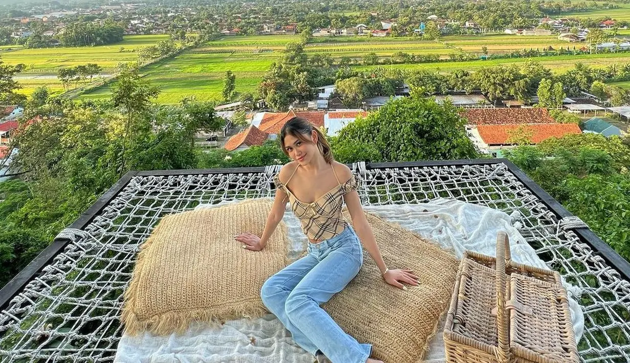 Berpose dengan latar pemandangan sawah, gunung, dan langit yang luar biasa indah, Belleza terlihat mengenakan crop top dengan tali spageti, dipadunya dengan celana jeans panjang. Foto: Instagram.