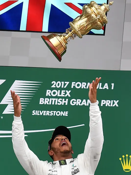 Lewis Hamilton melempar trofi diatas podium setelah berhasil memenangkan GP Inggris di sirkuit Silverstone, (16/7). Hamilton juga tercatat telah lima kali menjuarai GP Inggris (2008, 2014, 2015, 2016, dan 2017). (AFP Photo/Ben Stansall)