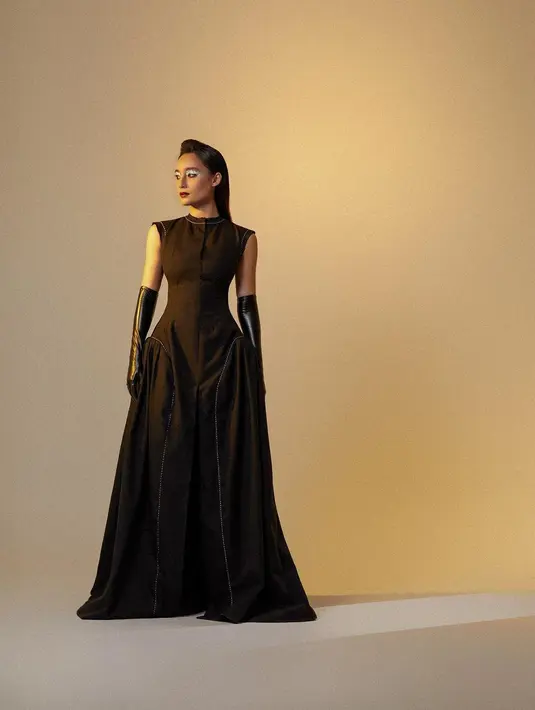 <p>Tampilan dramatis Tatjana Saphira kenakan gaun hitam rancangan Stella Rissa. Gaun tanpa lengan ini memiliki bagian rok yang mengembang ke bawah. Tatjana Saphira juga terlihat mengenakan gloves karet berwarna hitam dan menata rambutnya dengan gaya sleek, serta eye-makeup metalik yang semakin menyempurnakan penampilannya. Foto: Instagram.</p>