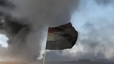 Sebuah bendera Irak terlihat di depan ladang minyak yang dibakar oleh ISIS di Qayyara, selatan Mosul, Irak, (23/11).Sebelumnya, sekitar enam sumur minyak telah dibakar ISIS di kawasan tersebut. (REUTERS/Goran Tomasevic)