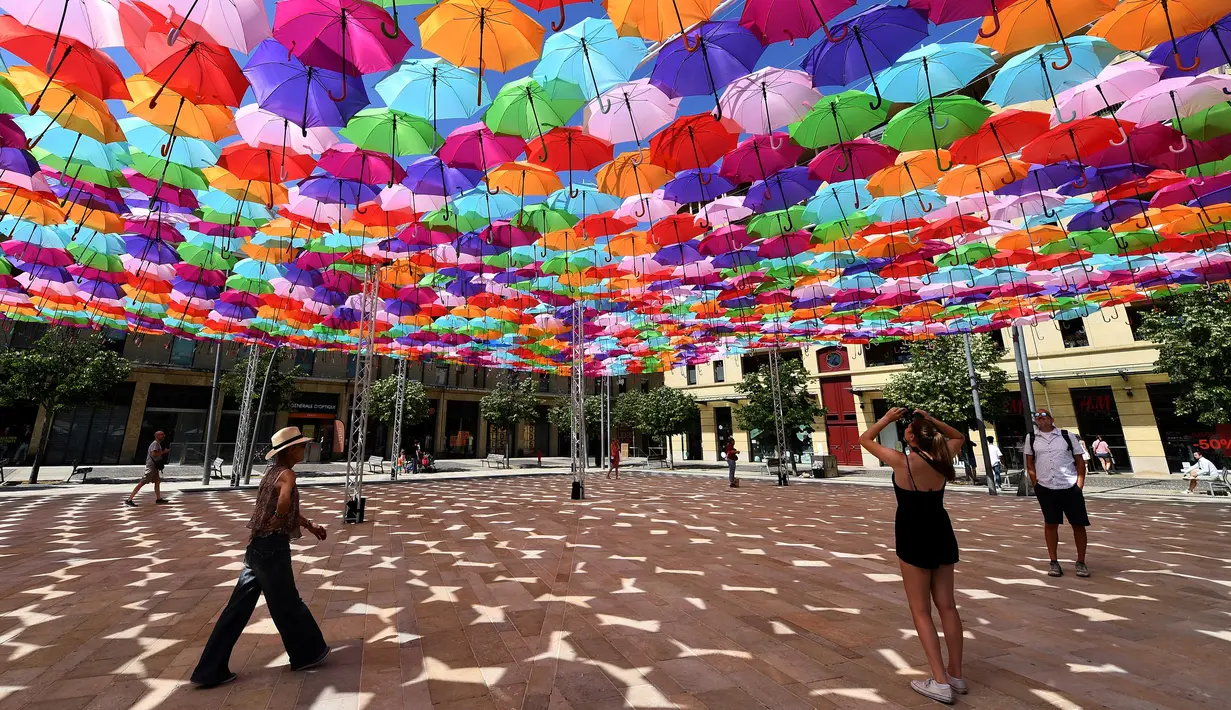 Pengunjung melewati instalasi Umbrella Sky Project di Aix-en-Provence, Prancis, Jumat (28/6/2019). Spot berteduh yang instagramable tersebut merupakan karya seniman Portugis Patricia Cunha. (BORIS HORVAT/AFP)