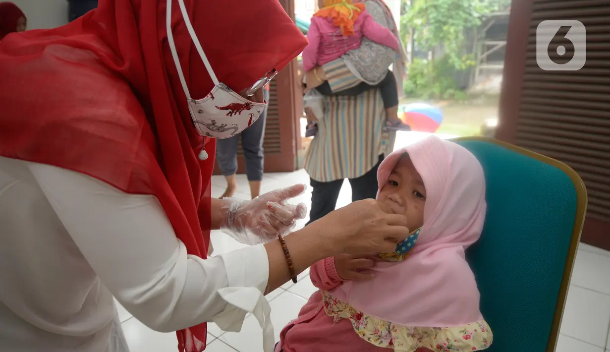 Bidan dibantu Kader Posyandu memberikan vaksin vitamin A dan imunisasi di Posyandu RW 20, Kelurahan Pondok Benda, Tangerang Selatan, Selasa (18/8/2020). Pemerintah sudah mengaktifkan pelayanan posyandu ketiga sejak pandemi Covid-19 dengan memperketat protokol kesehatan. (merdeka.com/Dwi Narwoko)