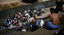 Orang-orang mengumpulkan air yang keluar melalui saluran pembuangan air limbah yang mengalir ke Sungai Guaire di Caracas, 11 Maret 2019. Pemadaman listrik selama berhari-hari di Venezuela berdampak terhadap krisis air. (REUTERS/Carlos Garcia Rawlins)
