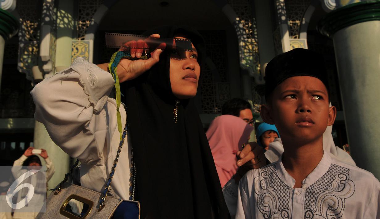 Warga menikmati proses Gerhana Matahari Total (GMT) menggunakan film bekas di halaman masjid Al-azhom Kota Tangerang, Rabu (9/3/2016). Salat gerhana tersebut diadakan sebagai ungkapan syukur atas kuasa Allah SWT. (Liputan6.com/Faisal R Syam)