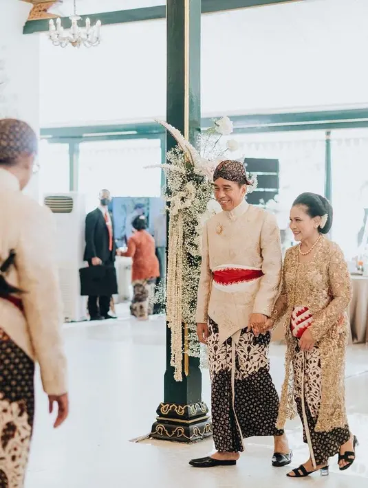 Potret gemas Pak Jokowi menggandeng tangan Ibu Iriana dibalut baju adat Jawa. Pak Jokowi mengenakan beskap putih bersiluet modern dengan bros emas di dada dan obi merah di pinggang, serta kain batik sebagai bawahan. Ibu Iriana tak kalah elegan berbalut kebaya emas panjang yang gemerlap dengan obi merah, dan kain batik yang serasi sebagai rok. [Foto: Instagram/doleytobing]