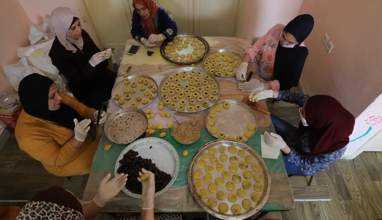 Para perempuan Palestina dengan masker dan sarung tangan menyiapkan biskuit tradisional menjelang Idul Fitri di sebuah rumah di kota tua Hebron, Tepi Barat yang diduduki, Selasa (19/5/2020). Biskuit-biskuit itu akan dijual secara online guna menjaga jarak selama pandemi Covid-19. (HAZEM BADER/AFP)
