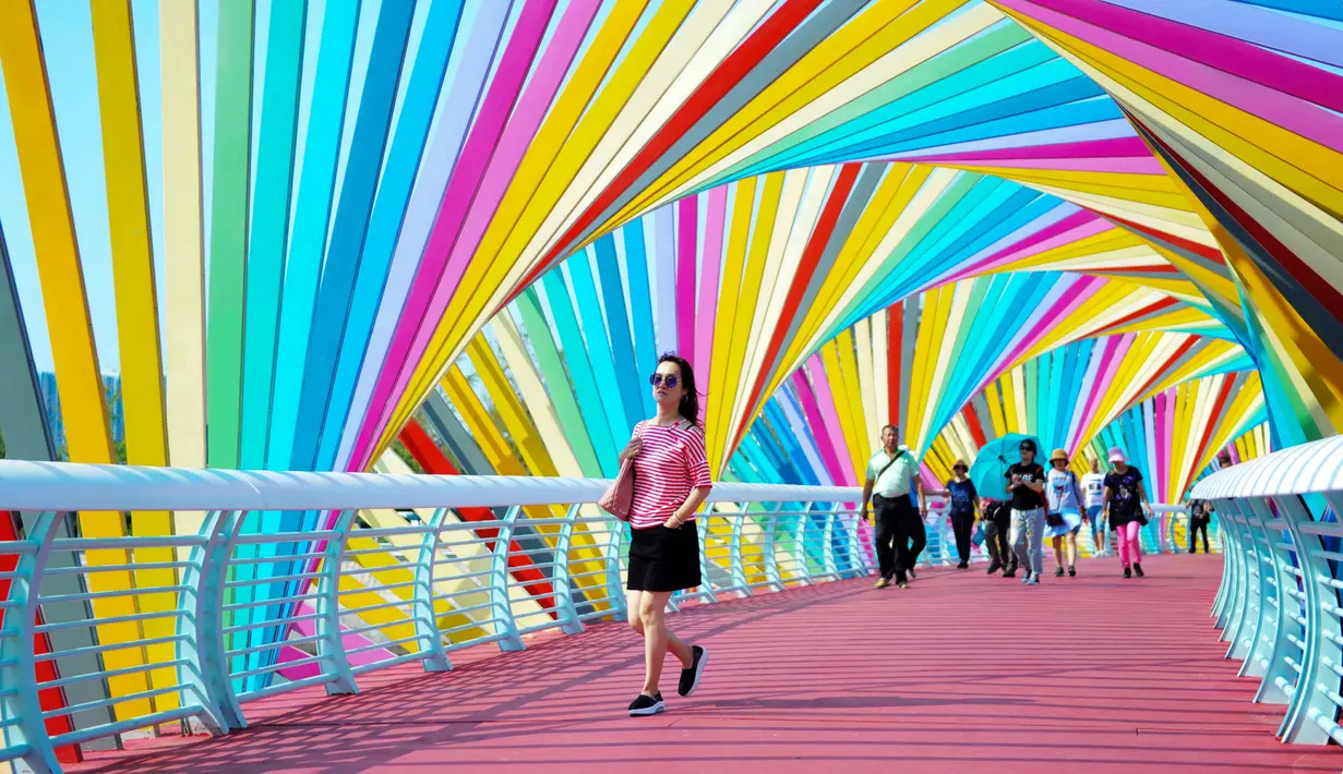 Warga berjalan melintasi jembatan warna-warni seperti pelangi yang berada di Qingdao, Shandong, China, Kamis (6/9). Jembatan pelangi ini terletak di Tangdaowan Seaside Park. (STR/AFP)