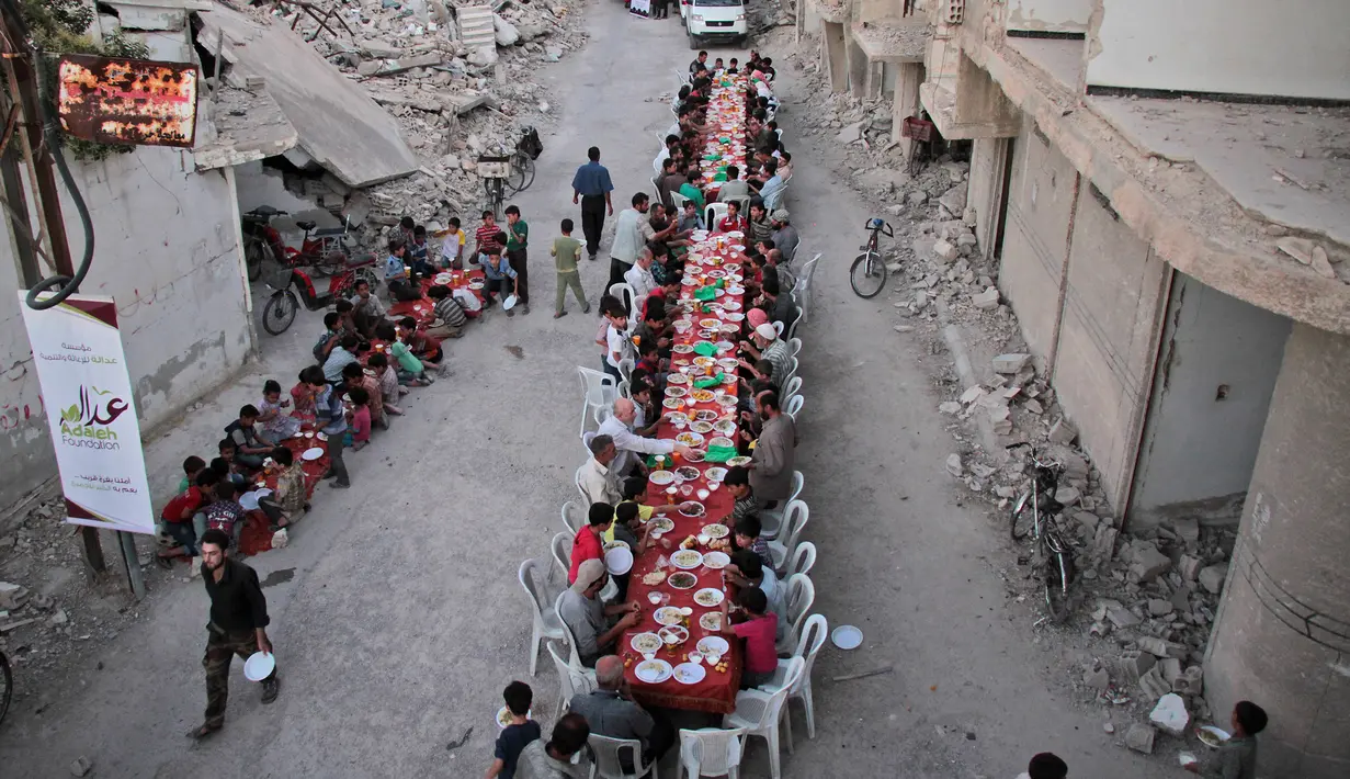 Suasana buka bersama Warga Suriah di tengah reruntuhan bangunan saat bulan suci Ramadan di Kota Douma yang dikuasai pemberontak di pinggiran ibukota Damaskus, Suriah, (18/6). (AFP Photo/Hamza Al-Ajweh)