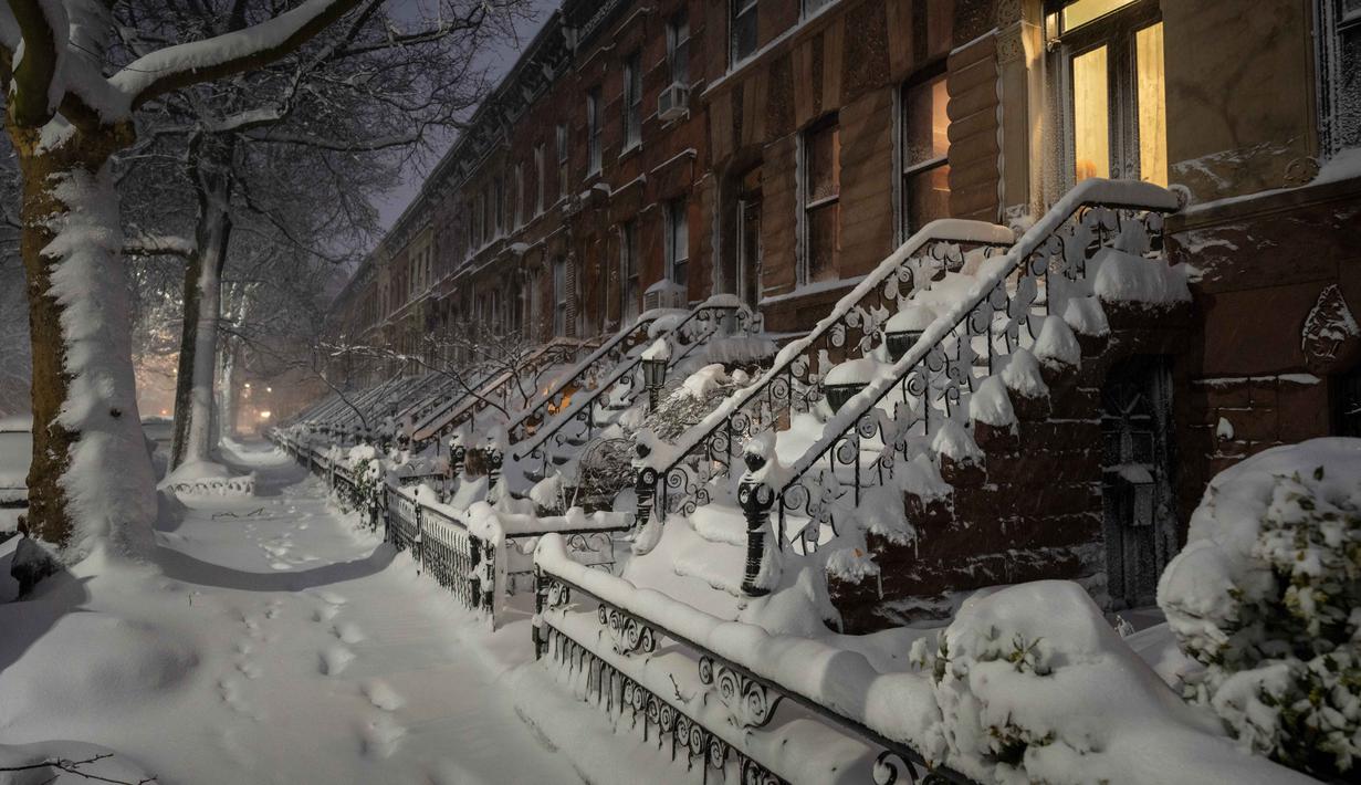 NWS juga mengeluarkan peringatan badai salju untuk Negara Bagian New York mulai pukul 13.00 waktu setempat pada Minggu (22/2/2026) hingga pukul 18.00 pada Senin (23/2/2026). Tampak dalam foto, salju menyelimuti bangunan-bangunan di distrik Brooklyn, Kota New York, sebelum matahari terbit pada Senin, 23 Februari 2026. (Jeremy Weine/Getty Images North America/Getty Images via AFP)