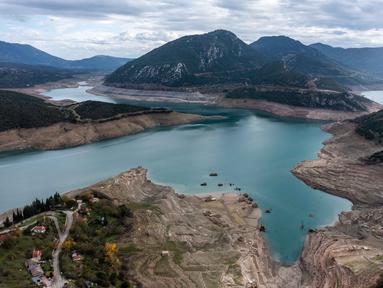 Foto ini menunjukkan sisa-sisa rumah yang muncul kembali ketika permukaan danau buatan Mornos menurun akibat kekeringan, di desa Kallio, sekitar 240 km barat laut Athena, Yunani pada 3 November 2025. Sebuah desa yang sudah tenggelam muncul kembali di Danau Mornos, Yunani pada 3 November 2025. (Angelos TZORTZINIS/AFP)