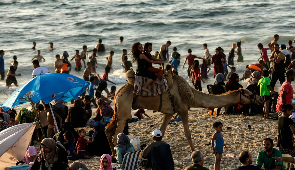 Warga Palestina naik unta mengelilingi pantai Kota Gaza, Jumat (22/6). Pantai Gaza menjadi pelipur bagi penduduk yang tak punya pilihan berwisata ke luar kota atau luar negeri. (AFP PHOTO/MAHMUD HAMS)
