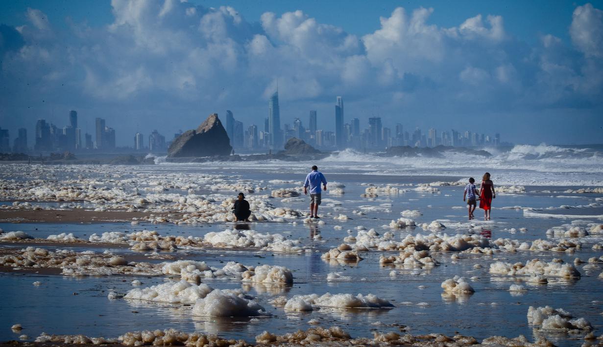 Turis berjalan di antara busa tebal setelah siklon tropis di Pantai Currumbin, Gold Coast, Australia pada 15 Desember 2020. Hujan lebat dan angin kencang telah melanda kawasan perbatasan padat penduduk antara New South Wales dan Queensland selama tiga hari. (Photo by Patrick HAMILTON / AFP)