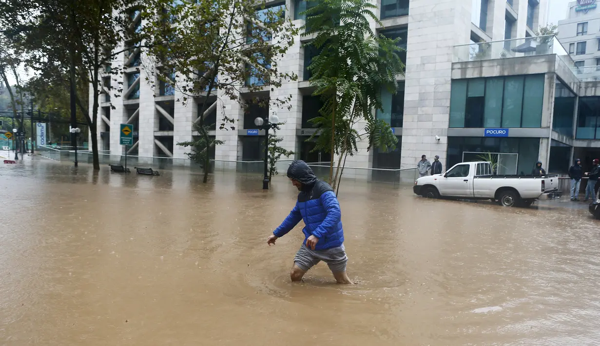 Warga melintasi jalan raya yang terendam banjir akibat hujan lebat dan parah di Santiago, Minggu (17/4). Tujuh orang hilang, 95 rumah mengalami kerusakan parah dan sekitar 80 orang kehilangan akses listrik akibat kejadian itu. (REUTERS/Ivan Alvarado)