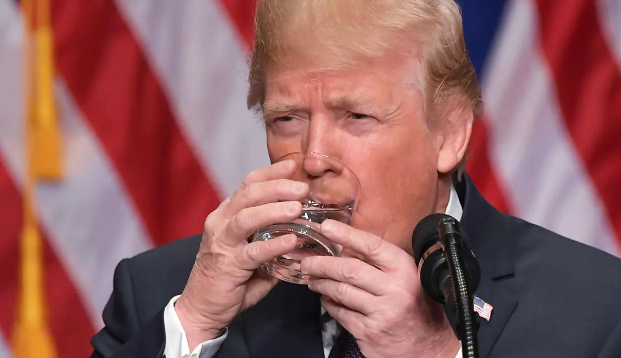 Presiden AS, Donald Trump saat meminum segelas air selama pidato keamanan nasional di Gedung Ronald Reagan di Washington, DC (18/12). Dalam pidatonya Trump menyatakan tentang strategi baru untuk Keamanan Nasional AS. (AFP Photo/Mandel Ngan)