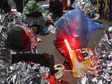 Para pendukung Presiden Korea Selatan yang dimakzulkan menggunakan selimut termal saat mengikuti aksi unjuk rasa di dekat kediaman Yoon Suk Yeol di Seoul pada tanggal 8 Januari 2025. (Anthony WALLACE/AFP)