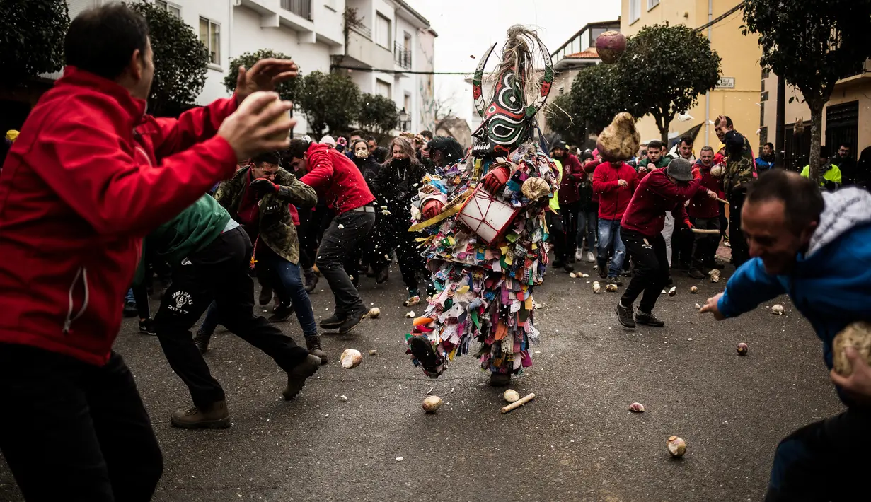 Orang-orang melempari seorang pria berkostum ala setan dengan sayuran lobak selama Festival Jarramplas di kota Piornal, Spanyol, Sabtu (19/1). Sembari dilempari lobak, sang Jarramplas tetap berjalan dan terus memukul drum yang dibawanya. (AP/Javier Fergo)