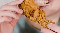 Seorang wanita sedang menggigit ayam kentucky. (Liputan6.com/Pexels/Tim Samuel)