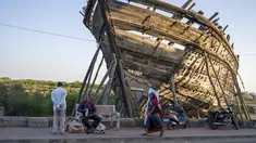 Seorang pedagang kaki lima duduk di bangku umum di depan haluan kapal tradisional yang sedang dibangun di Mandvi di Gujarat, India, Selasa (9/1/2024). (AP Photo/Ashwini Bhatia)