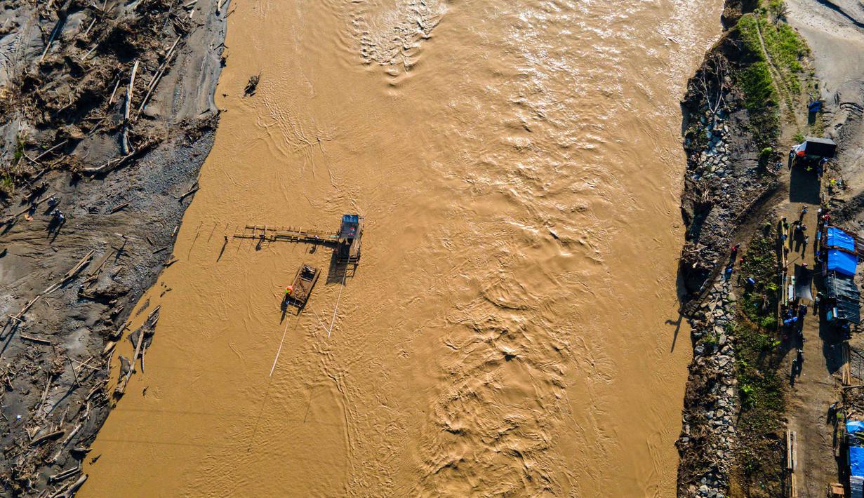 Rakit tali tersebut tak hanya mengangkut orang dewasa, tetapi juga sepeda motor. Tampak dalam foto, pemandangan udara menunjukkan orang-orang menyeberangi sungai Peusangan menggunakan rakit setelah banjir bandang yang menghancurkan desa-desa di sekitarnya di Kabupaten Bireuen, provinsi Aceh, pada Senin 5 Januari 2026. (CHAIDEER MAHYUDDIN/AFP)