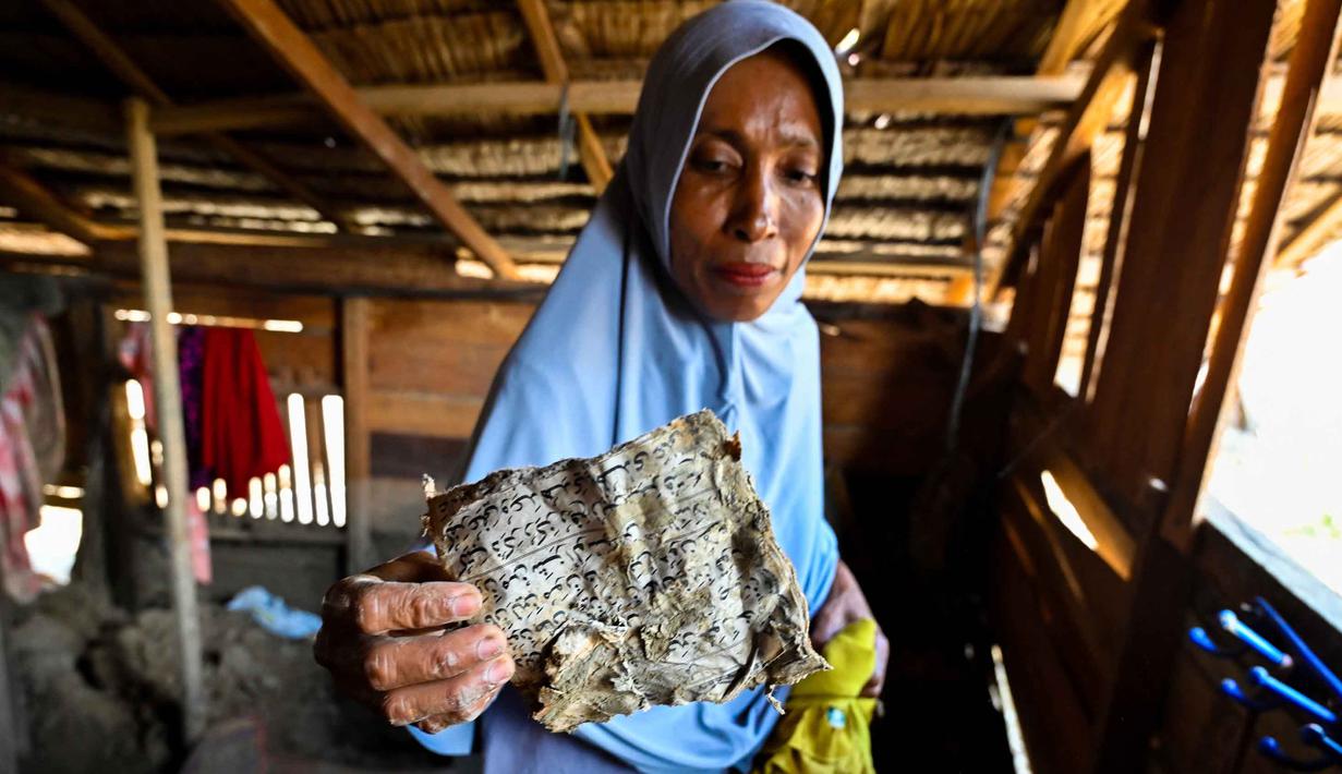 Warga berharap pembangunan dapat dipercepat agar mereka bisa segera pindah dari tenda darurat dan menjalani sisa Ramadan serta merayakan Idul Fitri di tempat yang lebih layak dan aman. Tampak dalam foto, Rauzah, seorang ibu empat anak yang selamat dari banjir, memegang halaman-halaman kotor dari buku yang digunakan anak-anak untuk belajar membaca Al-Quran, di rumahnya yang rusak di Meurah Dua, Kabupaten Pidie Jaya, Provinsi Aceh, pada 21 Februari 2026, setelah banjir dan tanah longsor dahsyat melanda Sumatra, akhir November 2025 lalu. (CHAIDEER MAHYUDDIN/AFP)