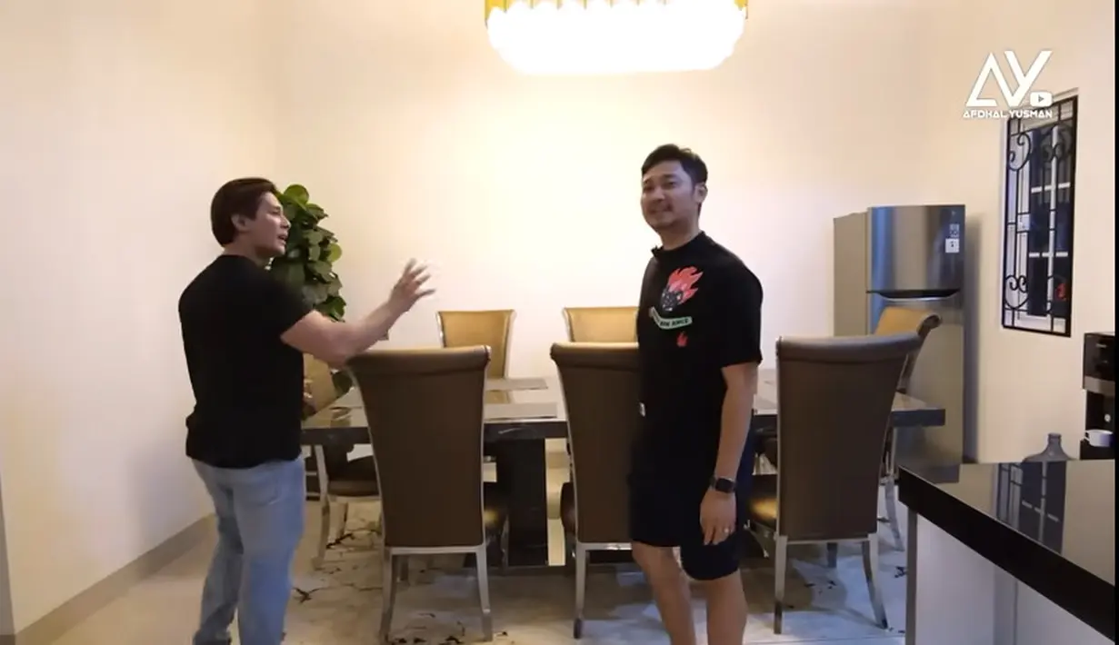 Tidak jauh dari living room terdapat ruang makan yang biasa digunakan untuk makan bersama. Terdapat beberapa kursi di meja panjang. Di sudut meja terdapat lemari pendingin dan tanaman hias di bagian pojok. [Youtube/Afdhal Yusman]