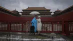 Pengunjung yang ditutupi jas hujan dan payung berdiri di gerbang masuk Kota Terlarang yang tertutup saat hujan badai membasahi Beijing, China, Minggu (30/7/2023). (AP Photo/Andy Wong)