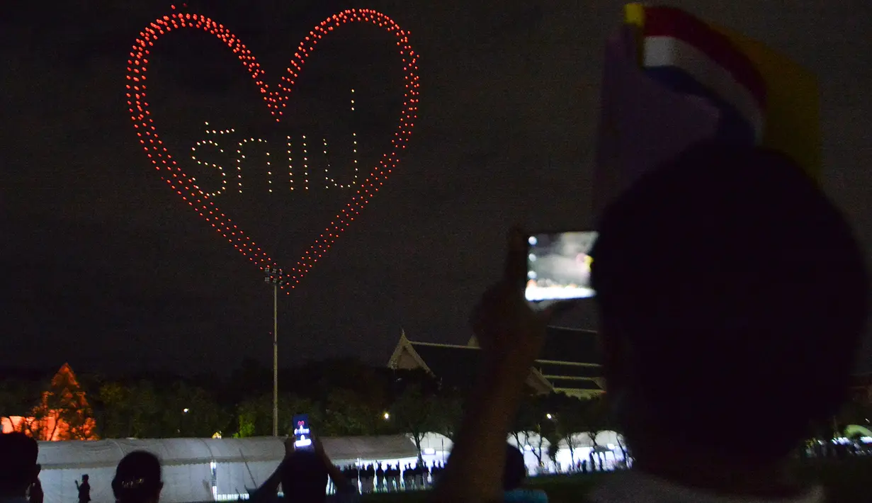 Orang-orang menyaksikan pertunjukan drone pada sebuah acara untuk merayakan ulang tahun ke-88 Ibu Suri Thailand, Ratu Sirikit, di dekat Grand Palace di Bangkok, Thailand, pada 12 Agustus 2020. (Xinhua/Rachen Sageamsak)