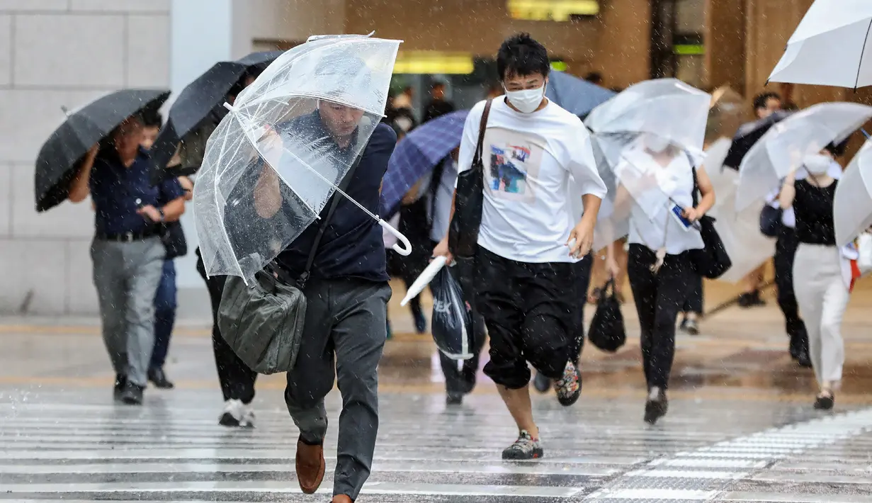 Pejalan kaki mencoba berlindung dari angin dan hujan saat mereka menyeberang jalan di depan Stasiun Osaka pada 15 Agustus 2023. (AFP/Jiji Press)