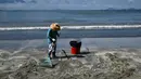 Seorang pria membersihkan sisa tumpahan minyak sawit dari pasir di sebuah pantai di Hong Kong, Senin (7/8). Sepuluh pantai di Hong Kong ditutup pada Minggu (6/8) setelah minyak sawit tumpah akibat tabrakan kapal di perairan China. (Anthony WALLACE / AFP)