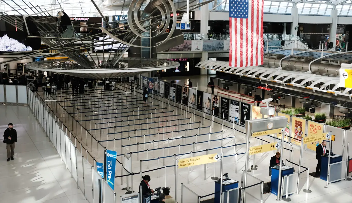 Orang-orang berjalan melalui terminal keberangkatan internasional yang sepi di Bandara John F. Kennedy (JFK), New York City, Sabtu (8/3/2020). Maskapai penerbangan terpukul wabah virus corona (COVID-19) setelah pelancong bisnis maupun rekreasi membatalkan rencana. (Spencer Platt/Getty Images/AFP)