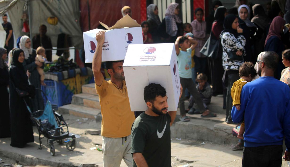 Pria-pria Palestina masing-masing membawa satu kotak makanan, yang dikumpulkan di pusat distribusi di kamp pengungsi Nuseirat, di pusat Jalur Gaza pada 2 November 2025. PBB menegaskan bahwa semua pihak harus menahan diri dari tindakan yang dapat membahayakan warga sipil dan pekerja kemanusiaan. (EYAD BABA/AFP)