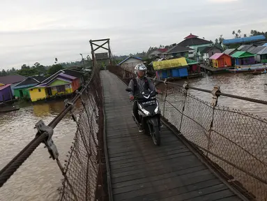 Warga melintasi jembatan penyeberangan di Sungai Martapura, Banjarmasin, Kalimantan Selatan, Selasa (27/3). Selain perahu, jembatan tersebut menjadi satu-satunya akses menyeberang bagi warga sekitar. (Liputan6.com/Immanuel Antonius)