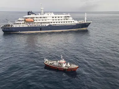 Pemandangan udara sebuah kapal ambulans yang membawa awak yang mengenakan pakaian pelindung bahan berbahaya (hazmat suit) saat mereka mendekati pintu kemudi di sisi kanan kapal pesiar MV Hondius, ketika kapal tersebut berhenti di lepas pelabuhan Praia, ibu kota Tanjung Verde, Selasa 5 Mei 2026. Kapal pesiar MV Hondius saat ini masih tertahan di lepas pantai Praia, Tanjung Verde. (Foto oleh AFP)